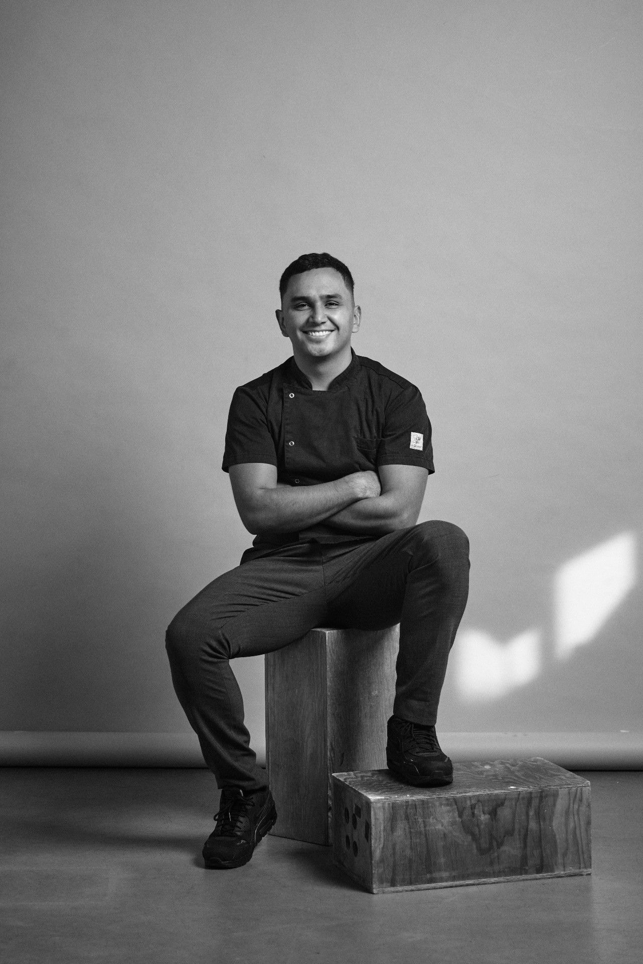 Retrato del anfitrión Julián Castro sentado con chaqueta de cocina, en blanco y negro