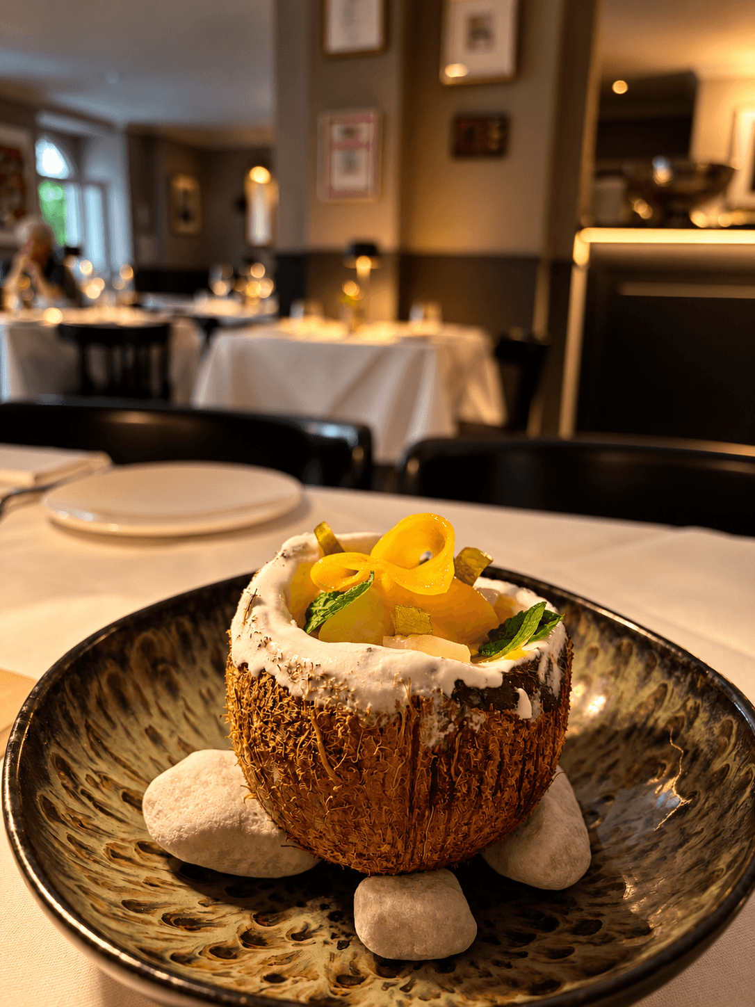 Postre servido en un coco, sobre cerámica con piedras blancas